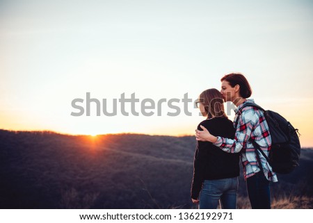 Mother kissing her daughter on a mountain peak at sunset