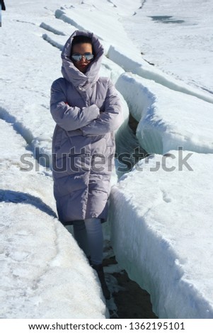 Girl in  warm down-padded coat enjoys a look at snow top. Winter fashionable shot.