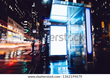 Bus station billboard in rainy night with blank copy space screen for advertising or promotional content, empty mock up Lightbox for information, blank display in urban city street with long exposure