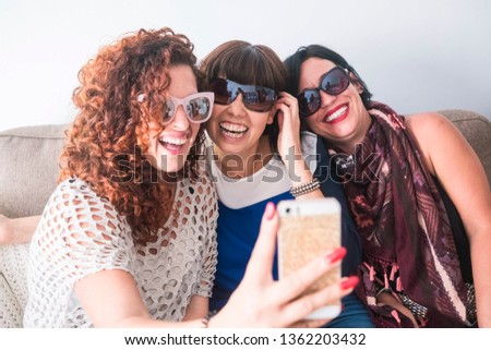 Three cheerful and crazy young women together in friendship have fun taking a selfie picture with a modern smart phone - laughing and smiling - group of females people with technology concept