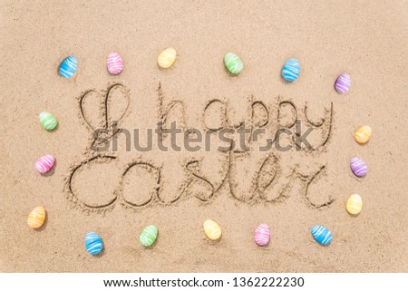 Happy easter background with eggs on the sandy beach near ocean. Hand drawn Happy Easter typography lettering sign.