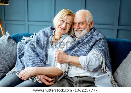 Portrait of a lovely senior couple feeling cozy and warm, sitting wrapped with plaid on the couch at home