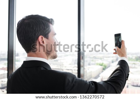 Business man in suit taking a selfie in office at panoramic window background