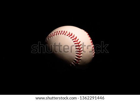 A close up of a white and red base ball in the dark with black background