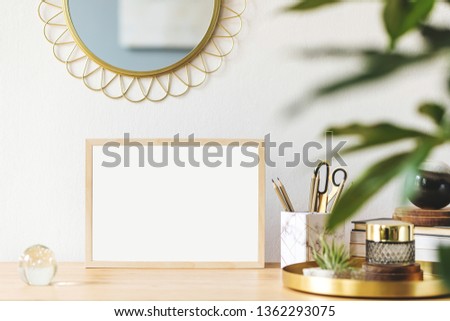 Stylish scanidnavian interior with mock up photo frame, design accessories and plants on the wooden desk. Beautiful mirror on the white wall. Creative desk of home decor. Warm and sunny room.