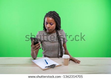 Lovely african young girl sitting at desktop and holding a smartphone