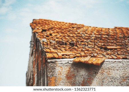 An old dilapidated tile roof of an abandoned rural house with orange shingles with some of them fell out of a regular roofing structure, strong warm sunlight, shallow depth of field, selective focus
