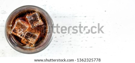 Top down view, glass with cola and ice cubes on white stone board - wide banner, space for text right