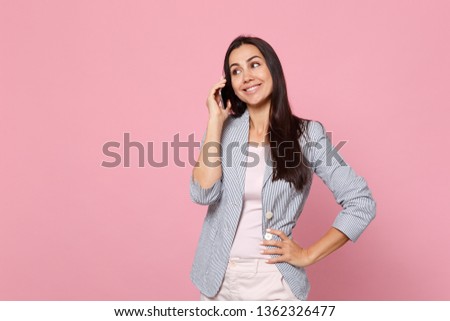 Smiling young woman in striped jacket talking on mobile phone, conducting pleasant conversation isolated on pink pastel wall background. People sincere emotions, lifestyle concept. Mock up copy space