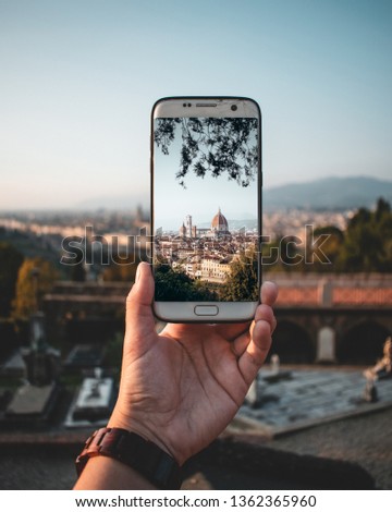 A white smartphone in the hand of a traveller taking a picture of the dome of Florence 