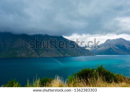 The mountains outside Queenstown, New Zealand on a cloudy day showing a small rainbow.