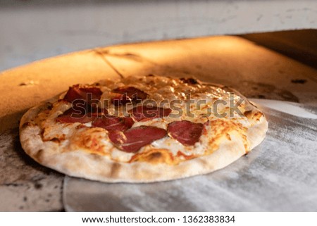 Cooked Truffle oil and Italian Dry-Cured Beef pizza on a metal pizza peel in an oven at a pizzeria.