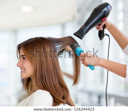 Beautiful woman at the hairdresser blow drying her hair Royalty-Free Stock Photo #136244423