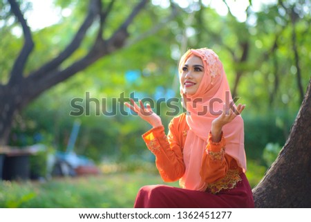 Portrait of colorful Muslim teenage girls wearing beautiful bright orange hijab in the natural atmosphere under the trees that provide clean air suitable for relaxation.
