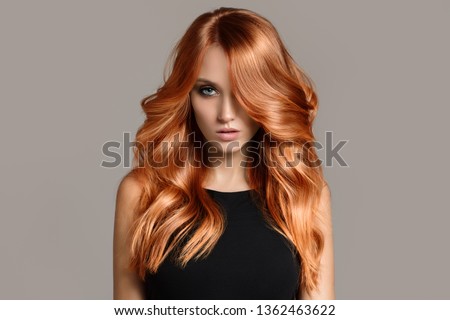 Beautiful woman with long wavy coloring hair. Flat gray background.