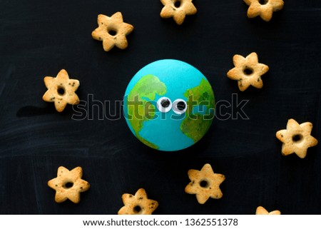 top view  handmade model  of Earth planet with funny googly eyes  and cookies in the shape of stars on the chalkboard , space and astronomy concept