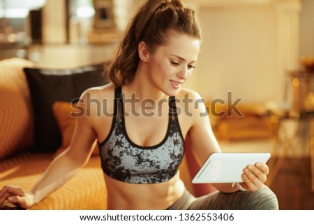 active woman in fitness clothes at modern home updating a fitness blog via tablet PC.