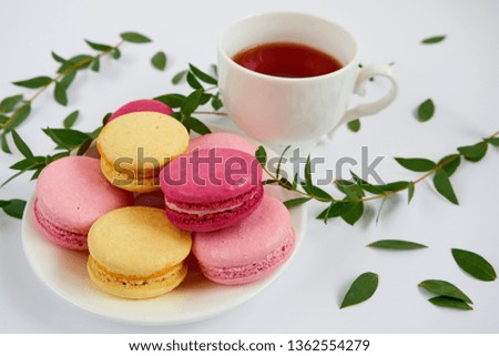 A cup of tea with a macarons on a white background, decorated with green leaves