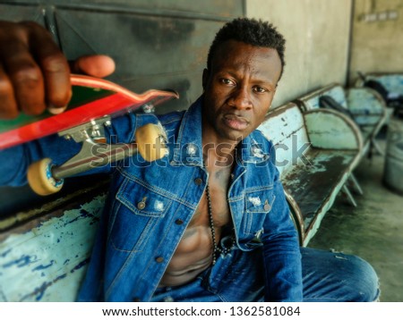 artistic portrait of young attractive and fit black afro American man sitting on corner street bench holding skate board posing in cool attitude in youth urban style and city lifestyle