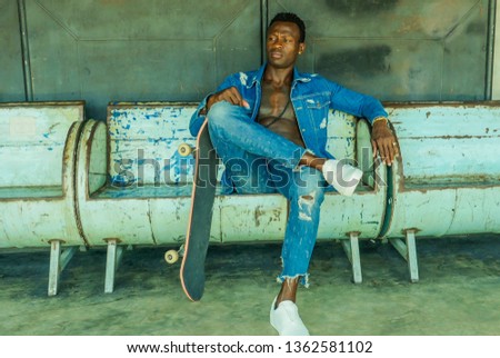 artistic portrait of young attractive and fit black African American man sitting on corner street bench holding skate board posing in cool attitude in youth urban style and city lifestyle