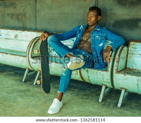 artistic portrait of young attractive and fit black African American man sitting on corner street bench holding skate board posing in cool attitude in youth urban style and city lifestyle
