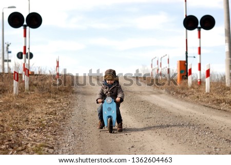 A little boy rides a bicycle near the railroad crossing. Dangerous fun.