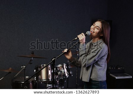 Young singer with microphone recording song in studio. Space for text
