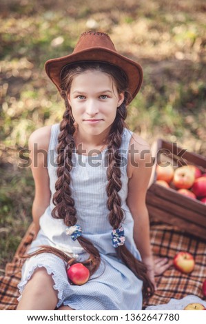 Girl with Apple in Apple Orchard. Beautiful Girl Eating Organic Apple in Orchard. Harvest Concept. Garden, teenager eating fruits at fall harvest. Apple pickking