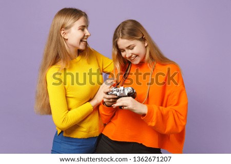 Two laughing young blonde twins sisters girls in vivid colorful clothes holding retro vintage photo camera isolated on violet blue wall background. People family lifestyle concept. Mock up copy space