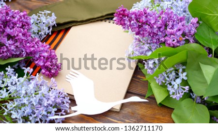 May 9 victory Day. Branches of blooming lilac for viewing, military cap, St. George's ribbon and a white paper crane on a wooden background / Cranes-the memory of the dead soldiers.Concept of memory.