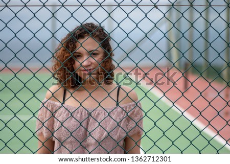 Smiling woman standing behind chainlink fence on tennis court