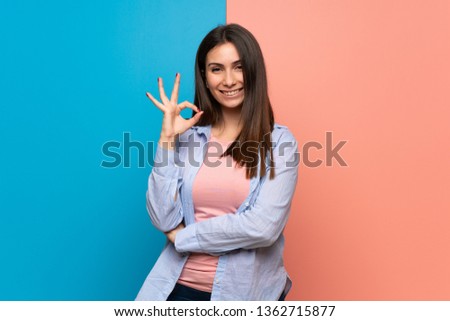 Young woman over pink and blue wall showing an ok sign with fingers