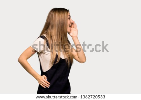 Young pretty woman shouting with mouth wide open to the lateral on isolated grey background