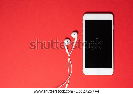 Smartphone with Blank Screen Connects to Earphones with Spiral Cable on Red Background Top View. Royalty-Free Stock Photo #1362725744