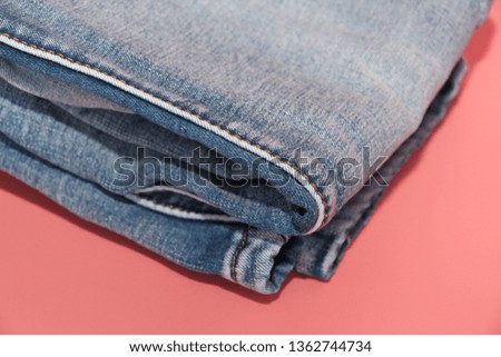 Folded blue jeans on a pink background. Faded blue jeans. Pink background.