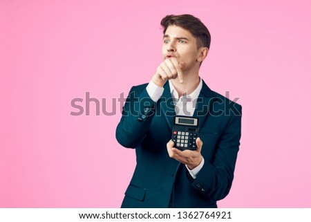 A virgin man in a suit on a pink background, puzzled, looks away and holds a calculator in his hand             