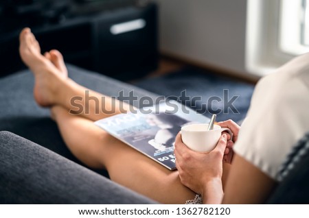 Sunday morning with magazine and coffee. Happy millennial woman relaxing with fashion and beauty trends news and cup of tea. Lady enjoying day off and me time on comfy couch. Fun weekend freetime. Royalty-Free Stock Photo #1362782120
