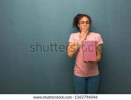 Young black woman tired and very sleepy. She is holding a popcorns bucket.