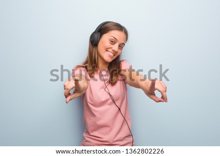 Young pretty caucasian woman cheerful and smiling pointing to front. She is listening to music with headphones.