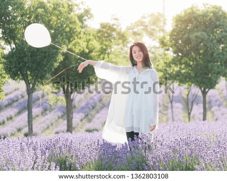 Beautiful young woman in white dress posing with helium balloon in hand in lavender field. Outdoor fashion portrait of glamour Chinese cheerful stylish girl enjoy her life in sunny day.