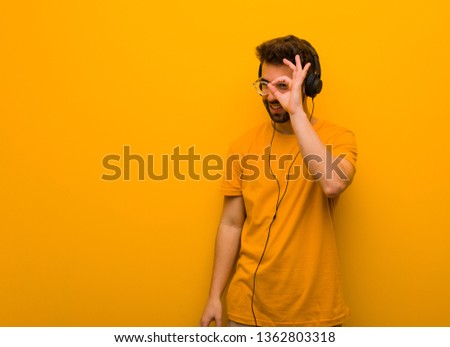 Young man listening to music confident doing ok gesture on eye