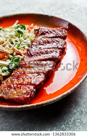 Traditional American barbecue pork ribs with a side dish of green salad. Grey background, side view