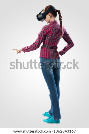 Beautiful girl using virtual reality glasses. Woman wearing VR goggles and interacts with cyberspace using pointing gesture. Studio photo by girl against gray background. Cyber technology concept