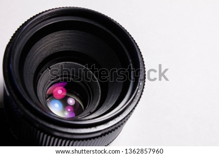 Black lens located on a white background. Multi-colored lights reflected in the lens in place of the diaphragm. Shutter concept, creativity and art in photography. Main equipment of the photographer.