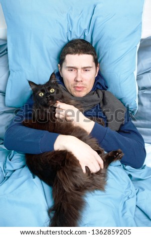 Photo of sick man in scarf with cat lying in bed