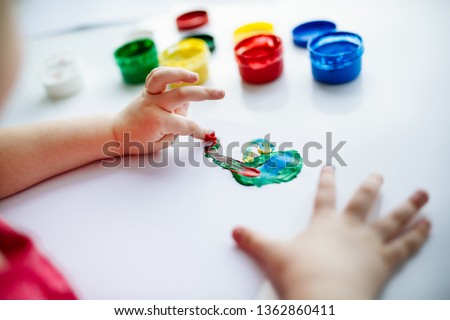 Kid hands start painting at the table with art supplies