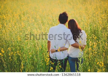 Asian couple happy and hugging in the yellow flower field.Lover standing in the romantic moment.Just marry young man and woman at the outdoor park.Black view sweet couple wedding on the garden view.