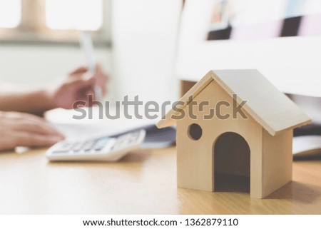 Wooden home model and key house on wood table with hand signing the document contract loan or mortgage property investment