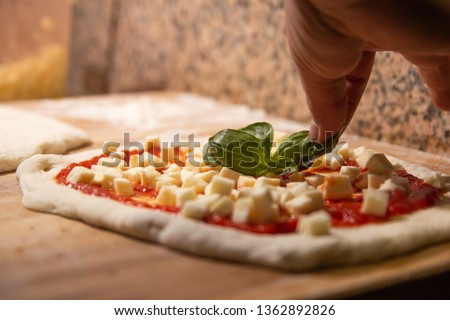Pizzaiolo's hand putting the basil on the Margherita pizza before being cooked