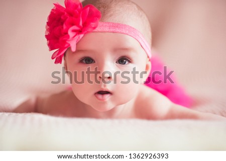 Funny baby girl wearing headband with flower lying in bed close up. Looking at camera. Childhood. 